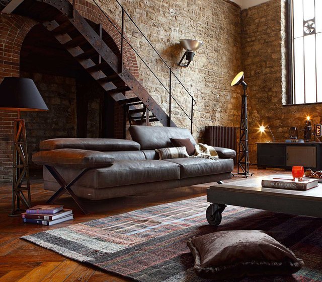 Căn phòng mang phong cách retro với chiếc ghế sofa da, thảm trải sàn lớn, bức tường đá và cầu thang sắt.