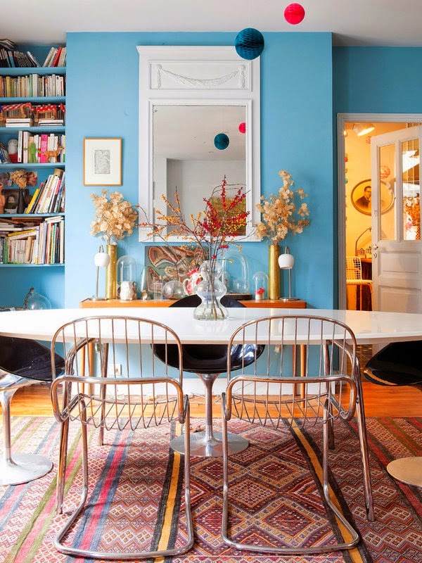 Những chiếc ghế được mix với nhau tạo nên bộ bàn ăn và điểm nhấn là thảm trải sàn nhiều họa tiết được đặt trên một tấm "background" là giá giá sách, kệ trang trí, gương treo tường với nhiều chi tiết, màu sắc.